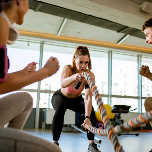 Trois personnes s'entraînent dans une salle de sport, utilisant une corde pour un cours de groupe dynamique.