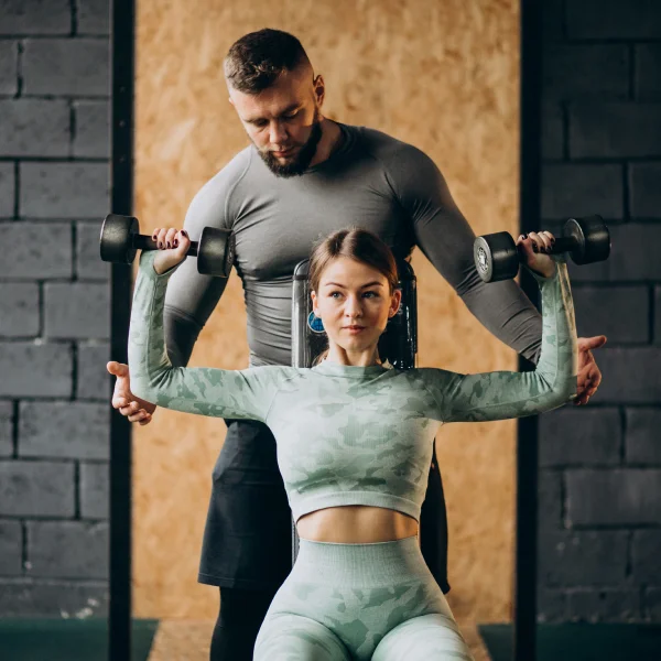 Un homme et une femme s'exercent avec des haltères sous la supervision d'un coach de fitness.