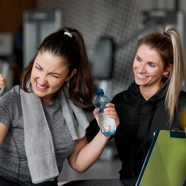 Deux femmes dans une salle de sport, tenant des bouteilles d'eau, participant à un programme de fitness.